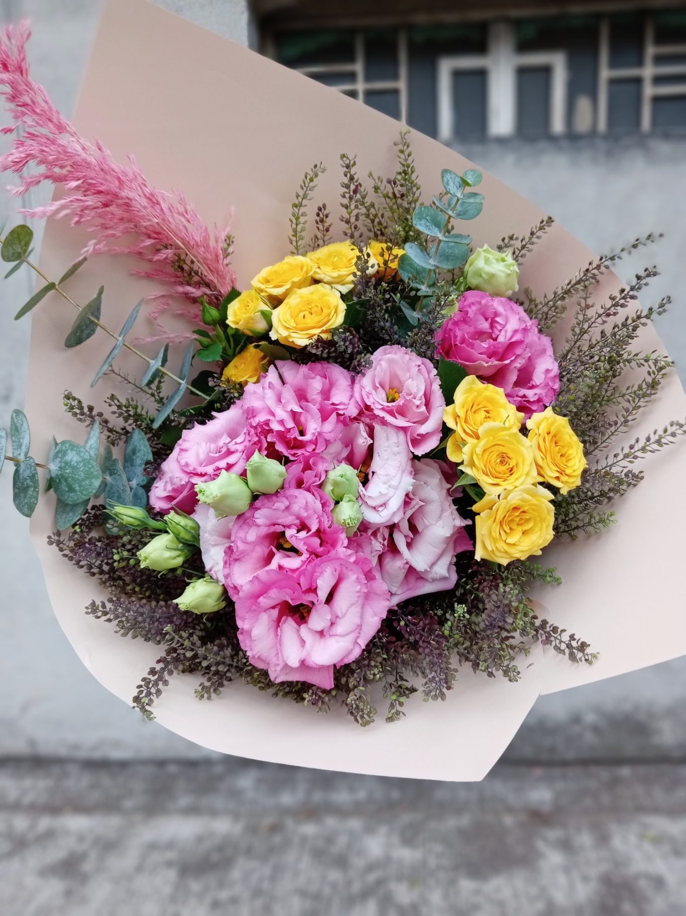 Ramo de flores con rosas rosas, claveles amarillos y eucalipto sobre fondo gris.