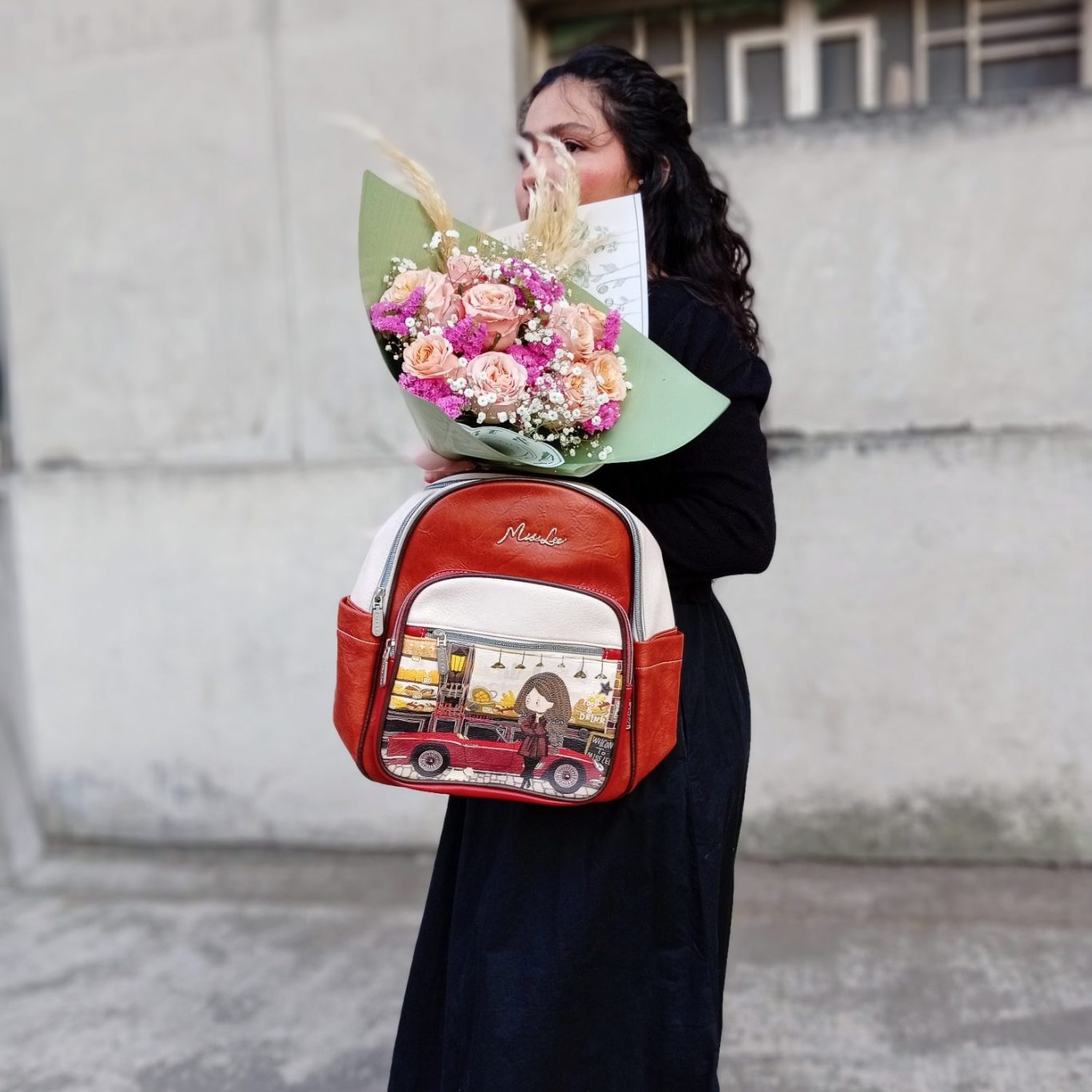 Mujer con cabello rizado sosteniendo un ramo de flores y una mochila de diseño colorida.