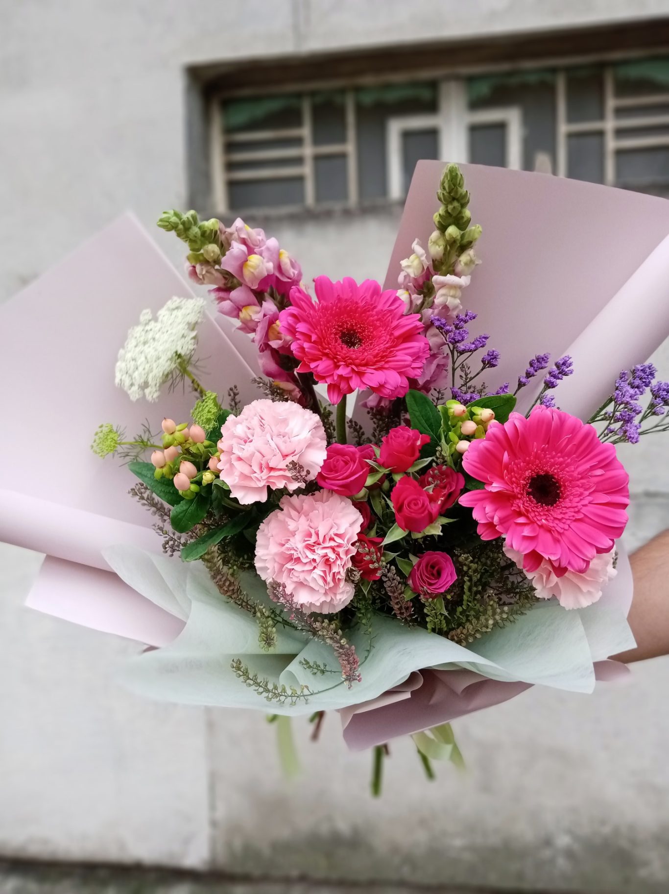 Ramo de flores coloridas con gerberas, claveles y otras flores en envoltura rosa.