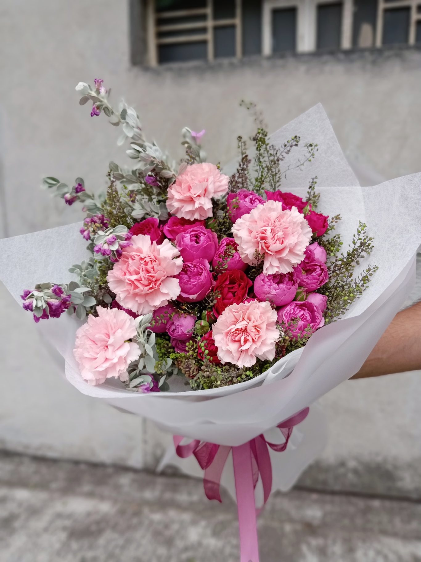 Ramo de flores con claveles rosa y púrpura, decorado con hojas verdes.