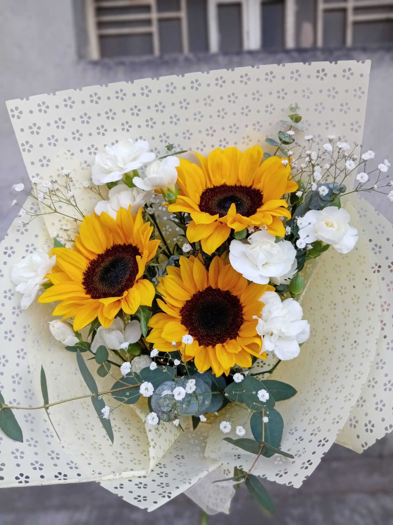 Ramo de girasoles y flores blancas sobre fondo claro, con papel decorativo.