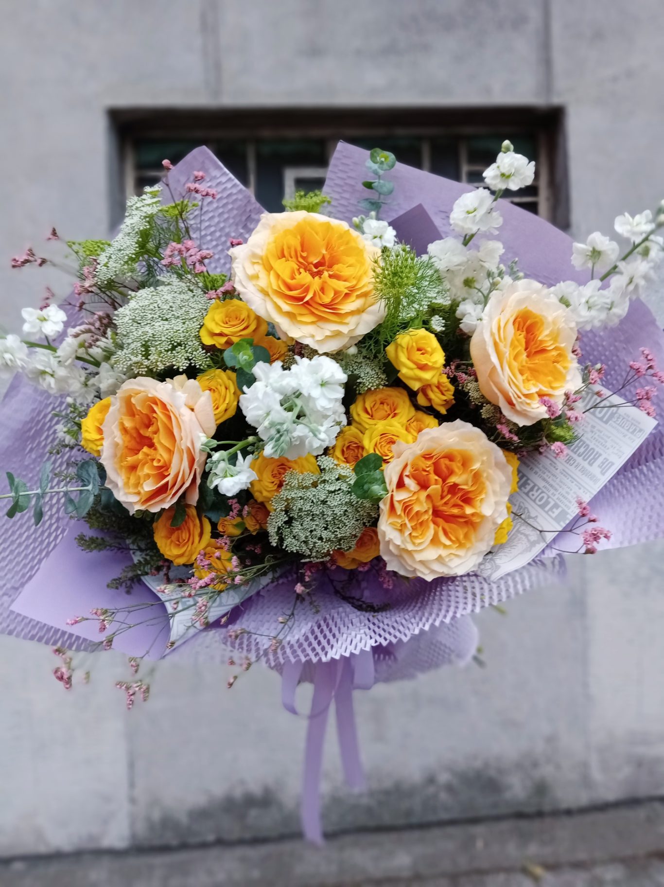 Ramo de flores con rosas naranjas y amarillas, además de otras flores blancas y verdes.