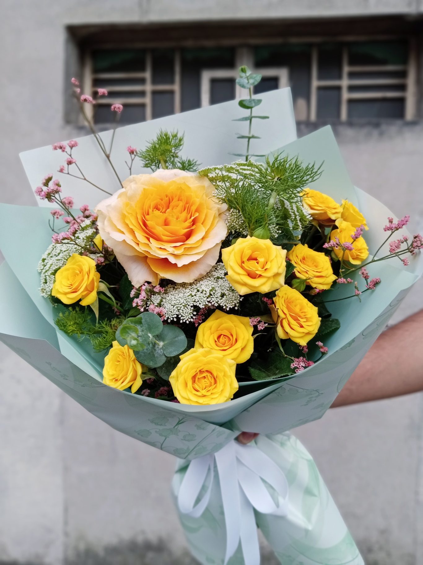 Ramo de flores con rosas amarillas y una rosa naranja, decorado con verdes.